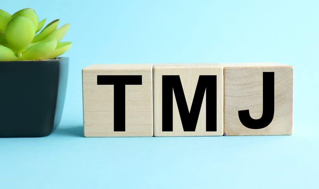 TMJ - acronym from wooden blocks with letters, abbreviation TMJ temporomandibular joint syndrome, TMD Temporomandibular disorder concept, random letters around, white background