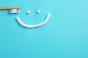 Smiling face made of toothpaste, brush and space for text on color background, top view