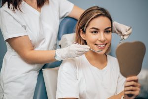 young and beautiful woman look at mirror after teeth treatment by professional dentist. Medicine concept