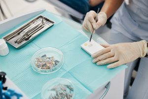 Hand in medical glove holding stainless steel double ended dental spatula and making filling from powder on foam plastic